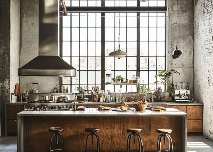 "Urban loft kitchen with industrial-style metal fixtures, rustic wooden cabinetry, high ceilings with exposed beams, and a large island with mismatched bar stools, illuminated by soft sunlight filtering through concrete walls, creating a cozy and modern vibe."